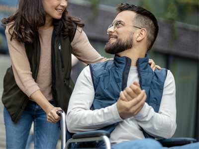 Jeune aide à domicile promenant une personne en fauteuil roulant.
